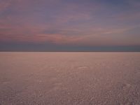 a lone lone white beach at sunset with purple skies in distance and lots of water