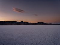 a large open plain with a sky and mountains in the background during sunset and dusk