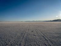 an open desert is seen from the ground in this image, which includes a lone person walking across a flat surface