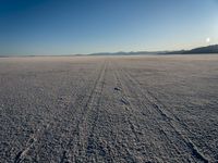 an open desert is seen from the ground in this image, which includes a lone person walking across a flat surface