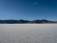 an empty empty desert plain under the blue sky with mountains behind it and a sky line in the distance