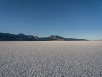 an empty empty desert plain under the blue sky with mountains behind it and a sky line in the distance