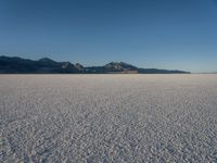 an empty empty desert plain under the blue sky with mountains behind it and a sky line in the distance