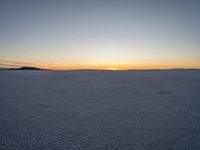 a person with a kite in the snow at sunset time that has a trail behind them