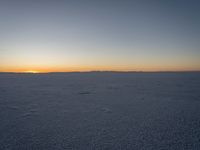 a person with a kite in the snow at sunset time that has a trail behind them