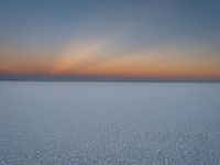 the sun is setting in the sky over the snowy field of ice snow is covered with snow