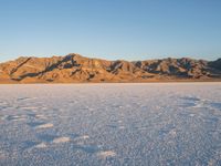 a lone person walks on the snow in a large landscape with mountains behind them and some rocks in the distance