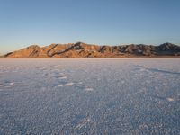 a lone person walks on the snow in a large landscape with mountains behind them and some rocks in the distance