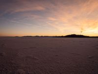 an orange sky is shown with the sun setting in the distance behind it and some footprints of footprints on the sand