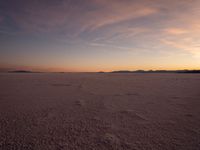 an orange sky is shown with the sun setting in the distance behind it and some footprints of footprints on the sand