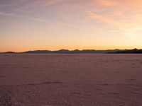 an orange sky is shown with the sun setting in the distance behind it and some footprints of footprints on the sand