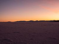 an orange sky is shown with the sun setting in the distance behind it and some footprints of footprints on the sand