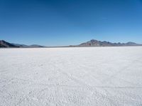 view of a vast snow landscape with mountains in the distance under a clear blue sky