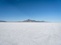 view of a vast snow landscape with mountains in the distance under a clear blue sky