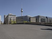 a boy skateboards across the bridge at berlin's tv tower, and some people are seen in the distance