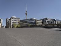 a boy skateboards across the bridge at berlin's tv tower, and some people are seen in the distance