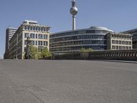 a boy skateboards across the bridge at berlin's tv tower, and some people are seen in the distance