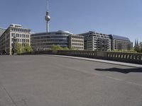 a boy skateboards across the bridge at berlin's tv tower, and some people are seen in the distance