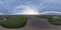 a fish eye lens view of a wide open area with houses and farm buildings with a sunset on the horizon