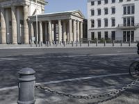 a woman riding a bicycle in the street next to some old buildings with pillars on each side and columns on either side