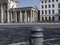 a woman riding a bicycle in the street next to some old buildings with pillars on each side and columns on either side