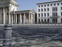 a woman riding a bicycle in the street next to some old buildings with pillars on each side and columns on either side