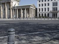 a woman riding a bicycle in the street next to some old buildings with pillars on each side and columns on either side