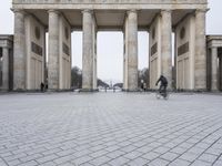 the people ride bicycles in front of the large building with many pillars and pillars behind it