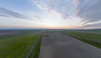 a sun is setting over an array of green fields with crops growing on the other side