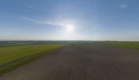 a sun is setting over an array of green fields with crops growing on the other side