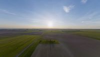 a sun is setting over an array of green fields with crops growing on the other side