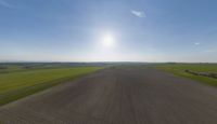 a sun is setting over an array of green fields with crops growing on the other side