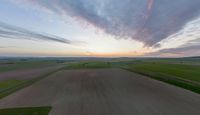 a sun is setting over an array of green fields with crops growing on the other side