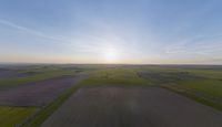 a sun is setting over an array of green fields with crops growing on the other side