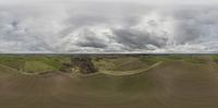 a field under cloudy skies in the daytime with a sky full of rain clouds over it