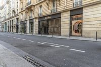 a person on a moped walks down an empty street with buildings behind them and a building to the right