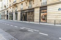 a person on a moped walks down an empty street with buildings behind them and a building to the right