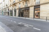 a person on a moped walks down an empty street with buildings behind them and a building to the right