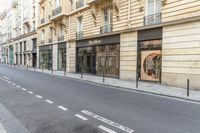 a person on a moped walks down an empty street with buildings behind them and a building to the right