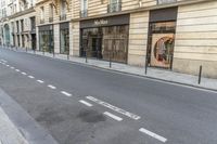 a person on a moped walks down an empty street with buildings behind them and a building to the right