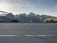 an empty parking lot with mountains in the background with a snow capped peak at the edge