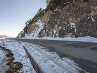 a narrow road next to the side of a snow covered mountain slope and an empty parking lot