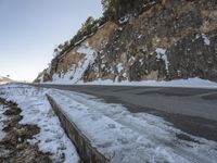 a narrow road next to the side of a snow covered mountain slope and an empty parking lot