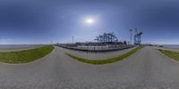 a fish eye lens view of the entrance to a beach park and parking lot, with trees and bushes at the shoreline