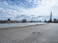 a brick walkway next to some water on a cloudy day looking out into the city