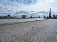 a brick walkway next to some water on a cloudy day looking out into the city