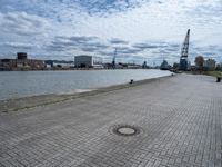 a brick walkway next to some water on a cloudy day looking out into the city