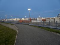 an empty street with traffic lights in the distance and large containers behind it at night