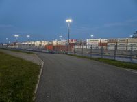 an empty street with traffic lights in the distance and large containers behind it at night