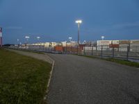 an empty street with traffic lights in the distance and large containers behind it at night